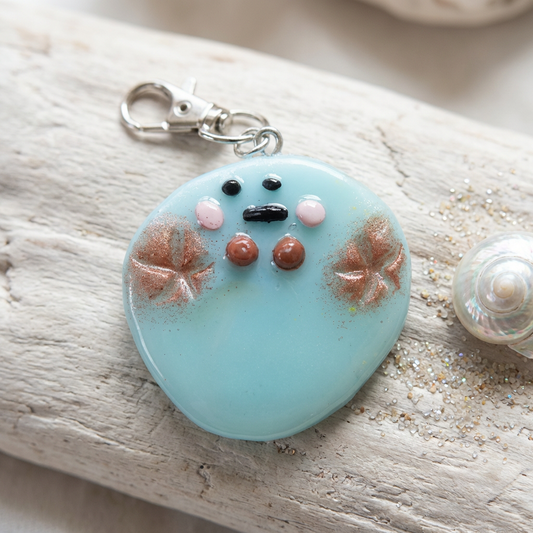 Glossy aqua polymer clay kawaii charm with a cute character face, shimmering gold starfish, and silver keychain clasp.